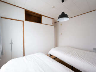 This minimalist bedroom features two twin beds with crisp white linens, perfect for a restful night's sleep.