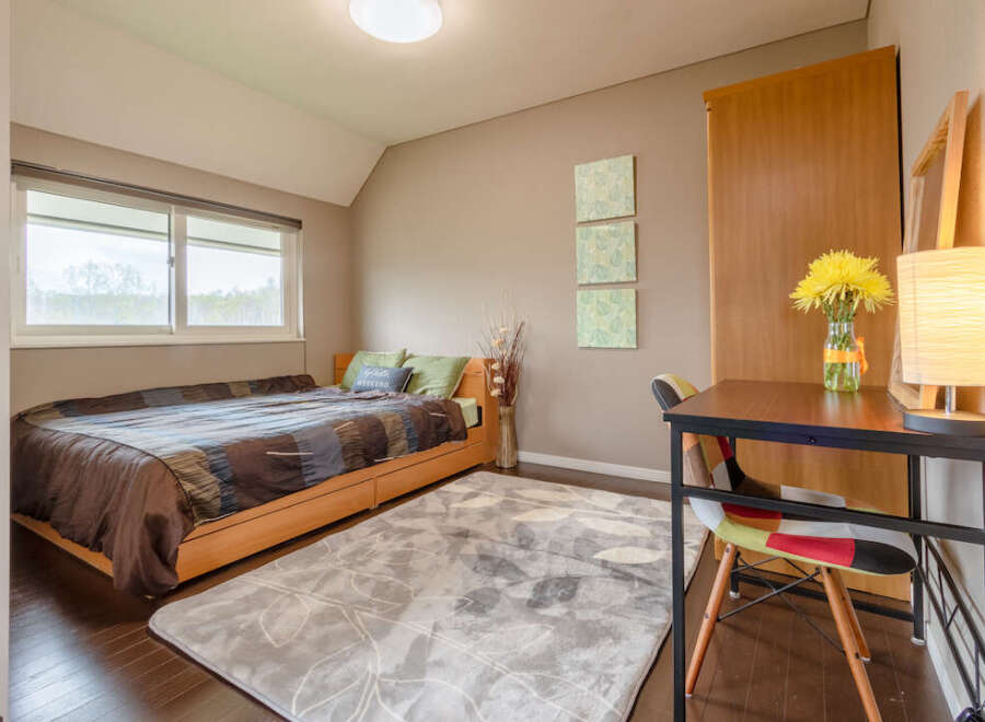 Cozy bedroom with a comfortable bed, a spacious desk perfect for working from home, and plenty of natural light from the large window.