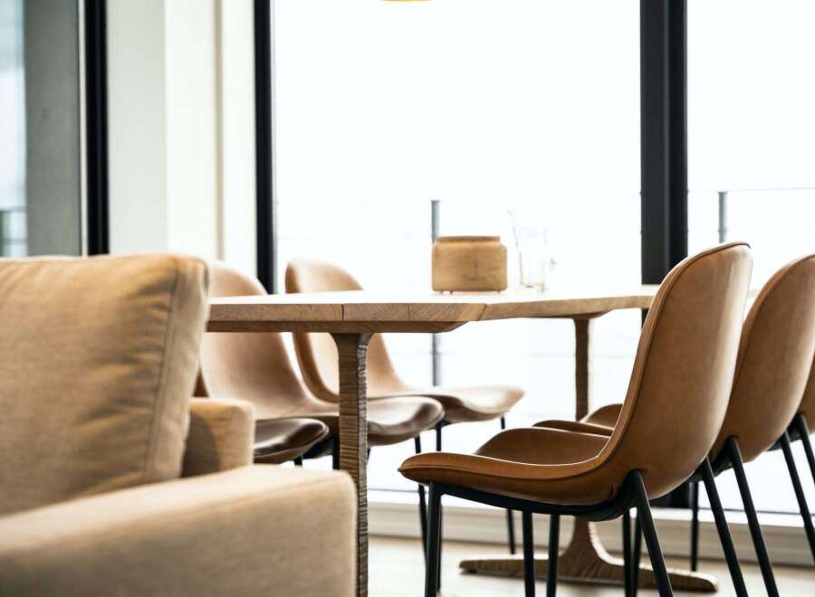 Modern living space featuring a light oak dining table with sleek black metal legs, surrounded by stylish tan leather chairs.
