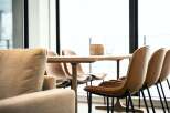Modern living space featuring a light oak dining table with sleek black metal legs, surrounded by stylish tan leather chairs.