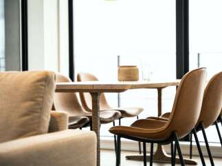 Modern living space featuring a light oak dining table with sleek black metal legs, surrounded by stylish tan leather chairs.