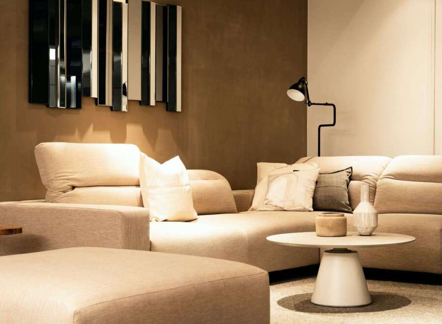Modern living room with beige sectional sofa and ottoman, complemented by a stylish mirror and floor lamp.