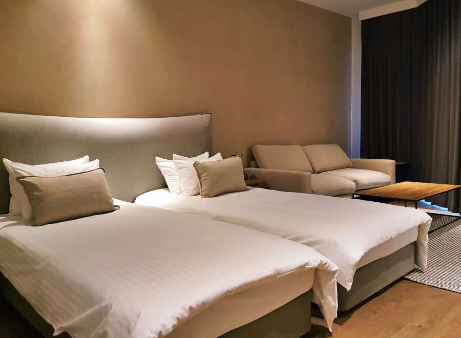 Relax in our stylish hotel room featuring twin beds with plush bedding, a comfortable sofa, and a modern coffee table.