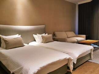 Relax in our stylish hotel room featuring twin beds with plush bedding, a comfortable sofa, and a modern coffee table.