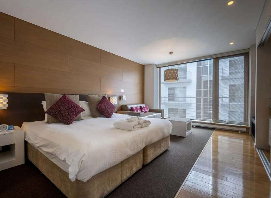 Modern hotel room with king-size bed, large windows offering city views, and stylish decor.