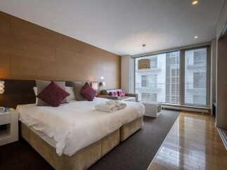 Modern hotel room with king-size bed, large windows offering city views, and stylish decor.