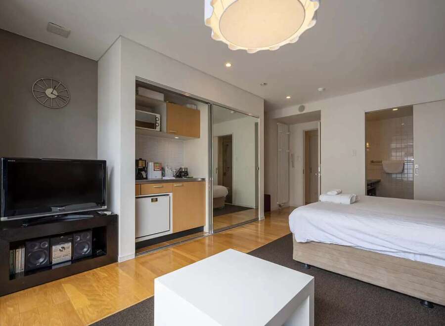 Modern studio apartment with mirrored sliding doors concealing a kitchenette and offering a bright, open feel.