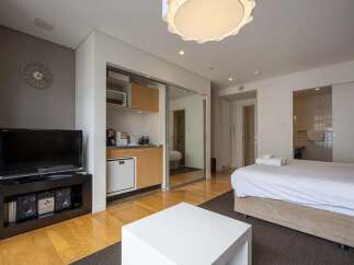 Modern studio apartment with mirrored sliding doors concealing a kitchenette and offering a bright, open feel.
