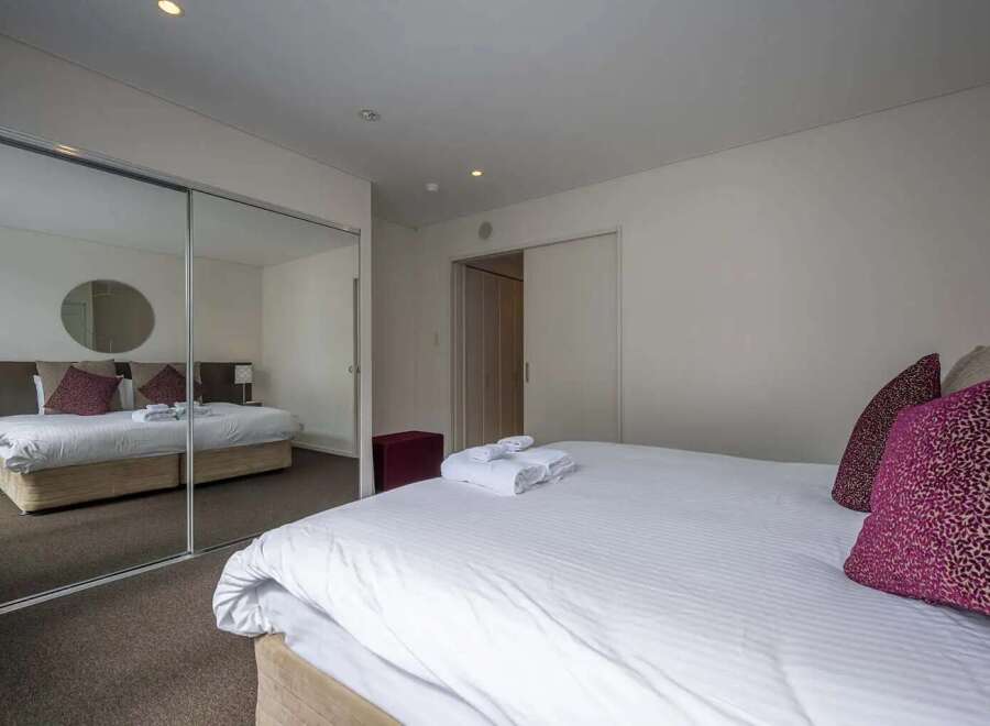 Modern bedroom with mirrored sliding doors, plush bedding, and ample closet space.