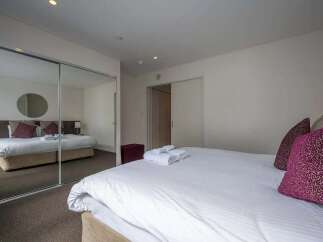 Modern bedroom with mirrored sliding doors, plush bedding, and ample closet space.