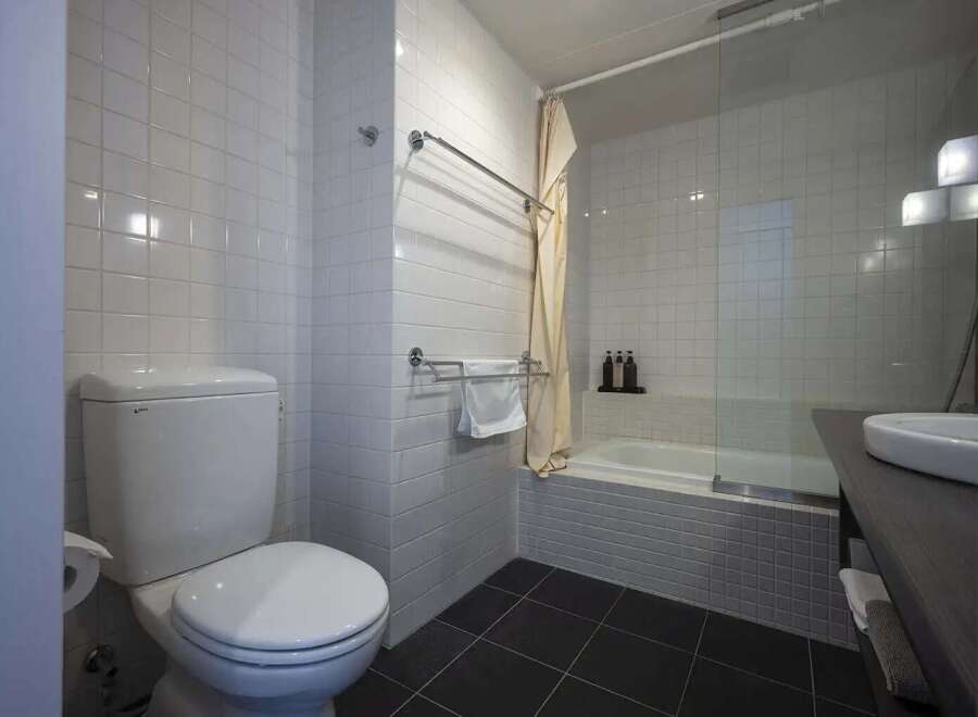 This modern bathroom boasts sleek white tile, a built-in bathtub with glass shower enclosure, and contemporary fixtures.