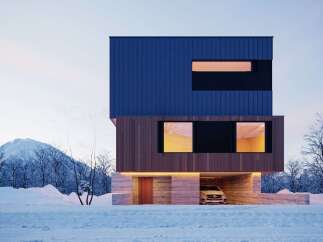 Stunning modern home nestled in a snowy landscape, featuring a sleek blue and wood exterior.