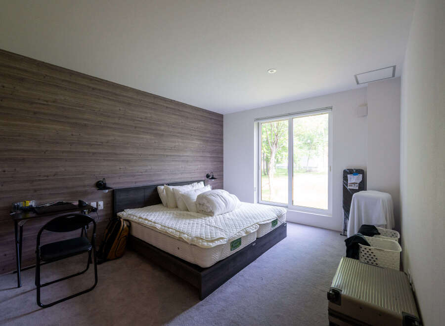 Modern bedroom with wood-paneled wall, comfortable queen-size bed, and large window overlooking a tranquil garden.