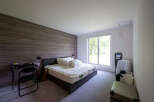 Modern bedroom with wood-paneled wall, comfortable queen-size bed, and large window overlooking a tranquil garden.