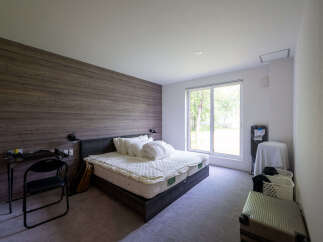 Modern bedroom with wood-paneled wall, comfortable queen-size bed, and large window overlooking a tranquil garden.