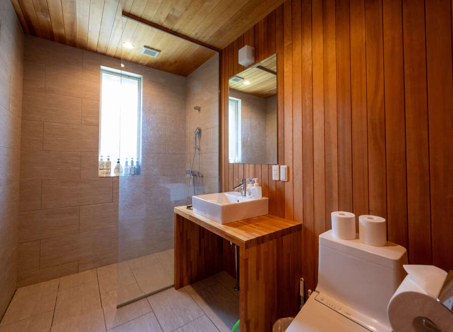 This modern bathroom boasts a sleek design with a glass shower enclosure, wooden wall paneling, and a stylish vanity.