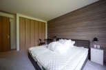 This modern bedroom boasts a cozy king-size bed with plush bedding, complemented by a sleek, dark wood wall and built-in closet.