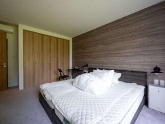 This modern bedroom boasts a cozy king-size bed with plush bedding, complemented by a sleek, dark wood wall and built-in closet.