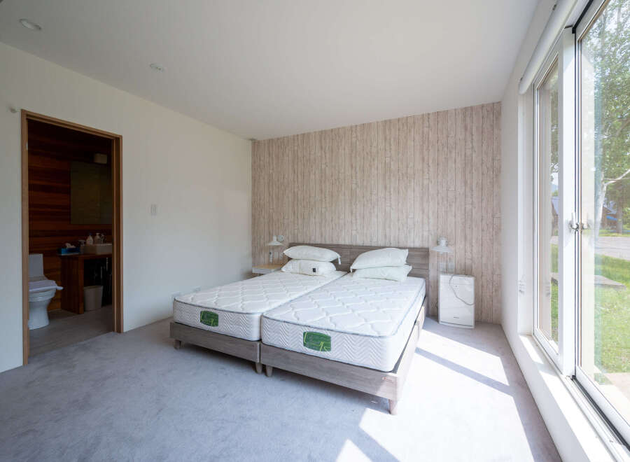Bright bedroom with twin beds, featuring a wood-like wall and large window offering natural light.
