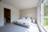Bright bedroom with twin beds, featuring a wood-like wall and large window offering natural light.