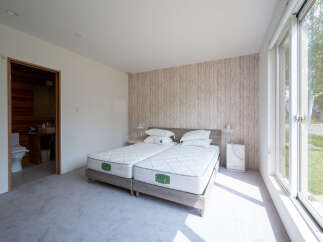 Bright bedroom with twin beds, featuring a wood-like wall and large window offering natural light.