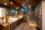 This stunning bathroom boasts a spacious shower with glass enclosure, dual sinks with wooden vanity, and a modern wooden ceiling.