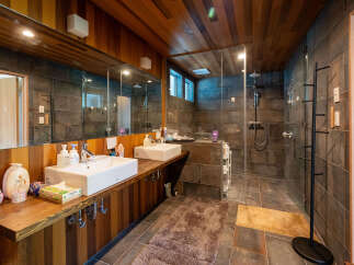 This stunning bathroom boasts a spacious shower with glass enclosure, dual sinks with wooden vanity, and a modern wooden ceiling.