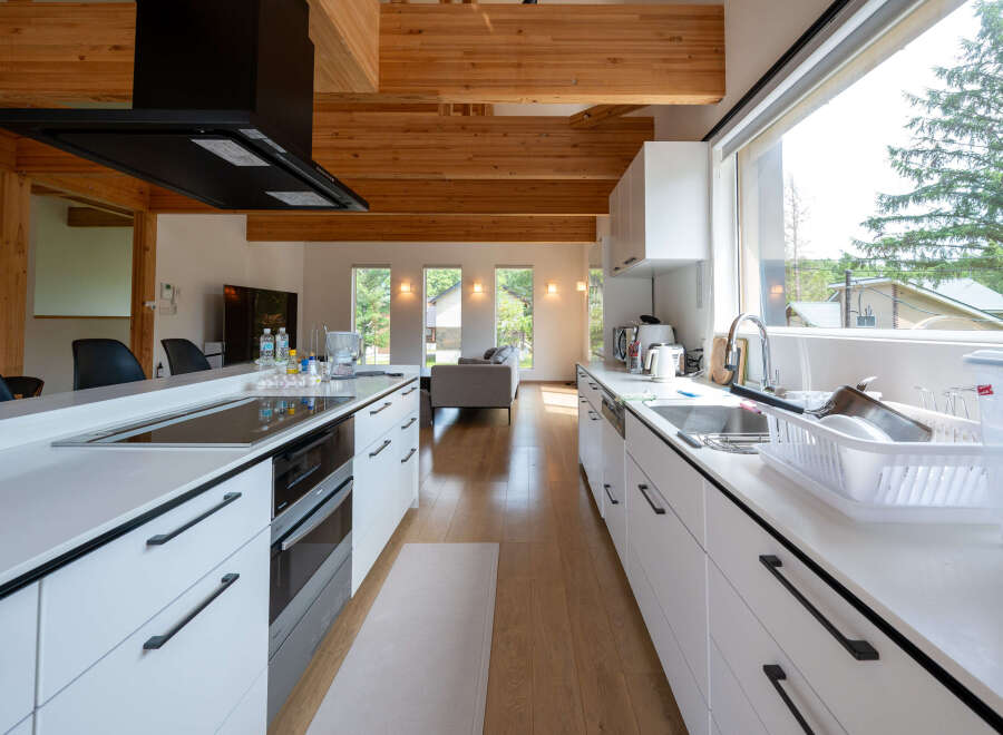 Modern kitchen with white cabinets and wooden beams, featuring a large island with built-in appliances and a spacious layout.