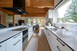 Modern kitchen with white cabinets and wooden beams, featuring a large island with built-in appliances and a spacious layout.