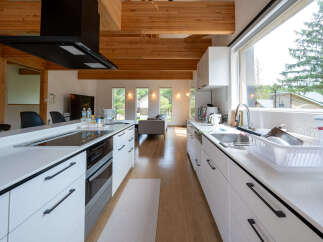 Modern kitchen with white cabinets and wooden beams, featuring a large island with built-in appliances and a spacious layout.