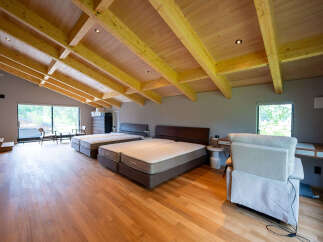 This stunning property boasts a spacious open-plan bedroom with high, exposed wooden beam ceilings and large windows offering abundant natural light.