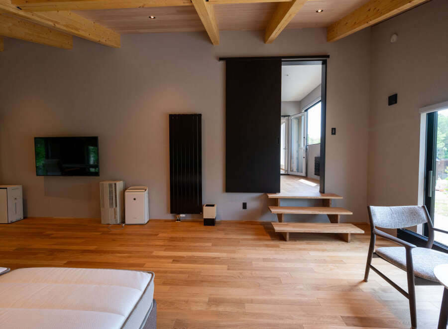 Modern minimalist living space with hardwood floors, exposed wooden beams, and floor-to-ceiling windows offering scenic views.