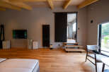 Modern minimalist living space with hardwood floors, exposed wooden beams, and floor-to-ceiling windows offering scenic views.