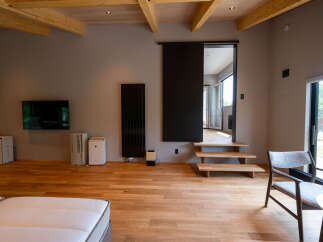 Modern minimalist living space with hardwood floors, exposed wooden beams, and floor-to-ceiling windows offering scenic views.