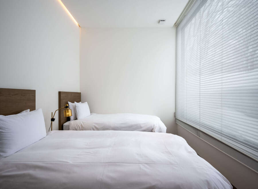 Modern minimalist bedroom with two twin beds, crisp white linens, and a sleek wooden headboard.