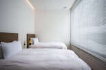 Modern minimalist bedroom with two twin beds, crisp white linens, and a sleek wooden headboard.