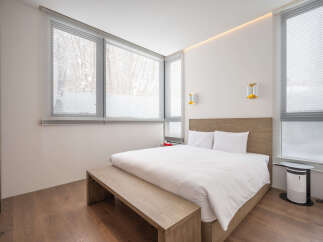 Modern bedroom with large windows offering natural light and views of snowy trees.