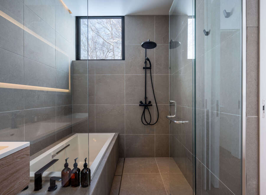 Modern bathroom with a sleek design, featuring a frameless glass shower enclosure, a built-in bathtub, and stylish black fixtures.