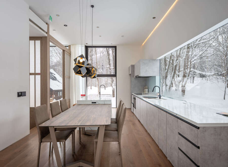 Modern kitchen and dining area with stunning views of a snow-covered forest.