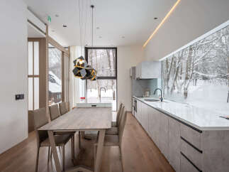 Modern kitchen and dining area with stunning views of a snow-covered forest.
