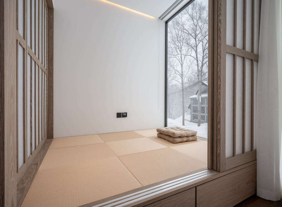 This serene bedroom features a minimalist design with tatami mats, shoji screens, and a stunning view of a snow-covered landscape.