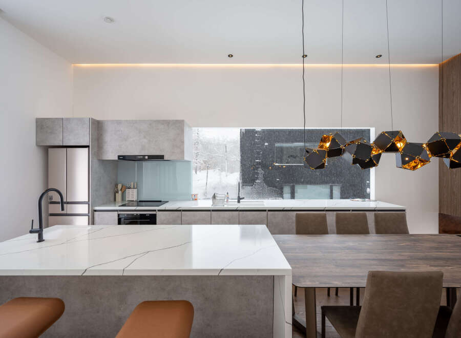 Modern kitchen with marble countertops and a large window overlooking a snowy landscape.