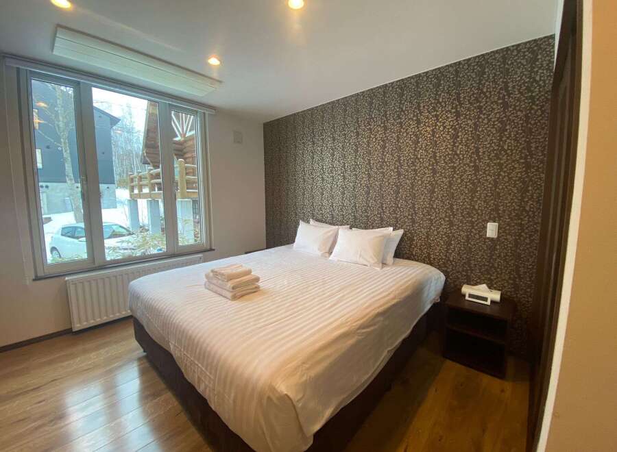 Cozy bedroom with a king-size bed, featuring a large window overlooking snowy scenery.