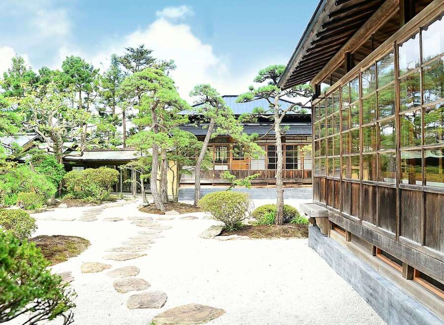 Discover serenity in this meticulously designed Japanese garden, featuring a traditional wooden house with expansive windows showcasing the lush greenery.