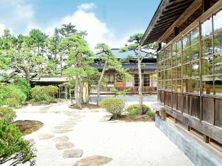 Discover serenity in this meticulously designed Japanese garden, featuring a traditional wooden house with expansive windows showcasing the lush greenery.