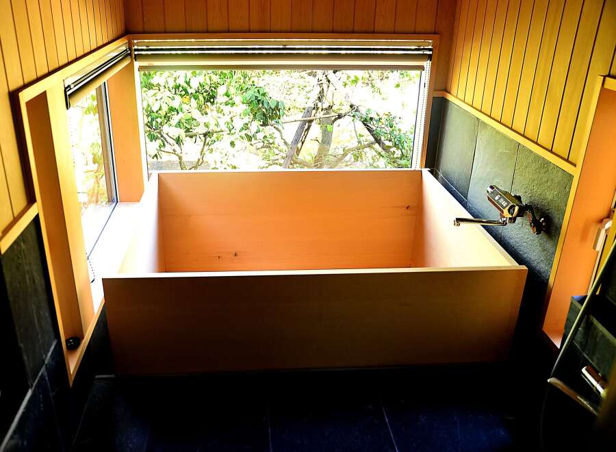 Relax in this luxurious wooden bathtub, nestled in a corner bathed in natural light from a large window overlooking lush greenery.