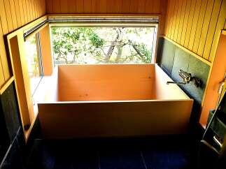 Relax in this luxurious wooden bathtub, nestled in a corner bathed in natural light from a large window overlooking lush greenery.