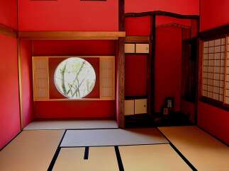 This serene Japanese-style room features tatami mats, shoji screens, and a circular window offering a tranquil garden view.