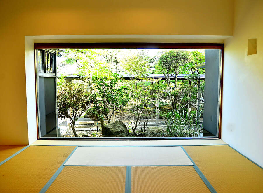 This serene room features tatami mats and a large window showcasing a meticulously landscaped Japanese garden.