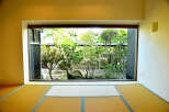 This serene room features tatami mats and a large window showcasing a meticulously landscaped Japanese garden.